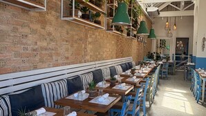 A restaurant with long wooden tables, blue chairs, striped benches, and hanging green pendant lights. - Renovated aparthotel located in the vibrant Ipanema district of Rio de Janeiro.  (Ipanema Rio de Janeiro)