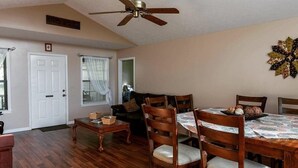 Un coin repas avec des chaises et une table en bois, un ventilateur de plafond et un élément décoratif fixé au mur.