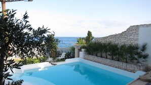 A swimming pool with a stone wall and plants, overlooking the sea. - A Slice of Heaven by the sea - Beahost Rentals (Syracuse)