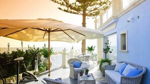 An outdoor patio with wicker furniture, a stationary bike, and a large umbrella. - A Slice of Heaven by the sea - Beahost Rentals (Syracuse)