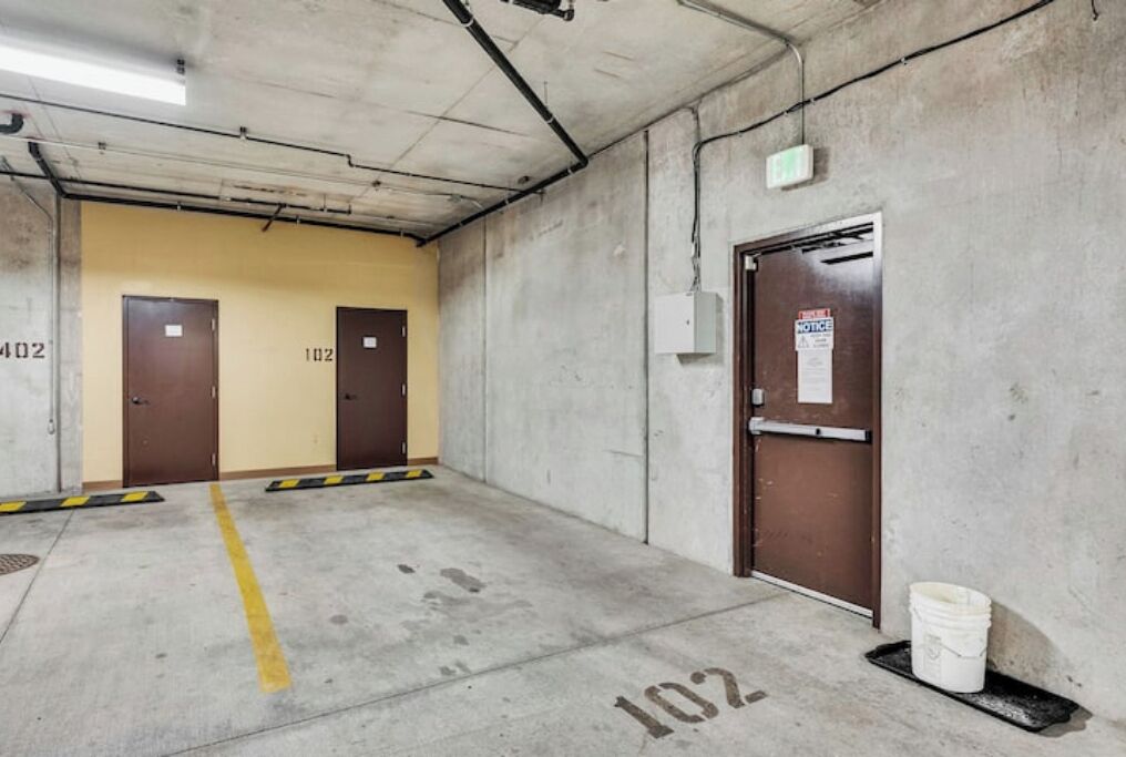 Un parking avec des murs en béton, deux portes portant l’inscription « 102 », et une ligne jaune peinte sur le sol.