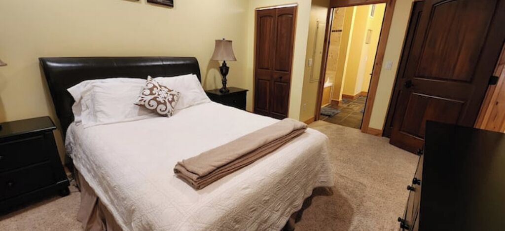 A neatly made bed with a white comforter and a folded blanket, a bedside lamp, and a wooden nightstand.