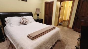 A neatly made bed with a white comforter and a folded blanket, a bedside lamp, and a wooden nightstand.