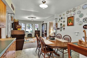 A dining area with a wooden table and chairs, a kitchen with wooden cabinets, and a wall decorated with plates. - Miner's Home by Kannegaard with Pool Table and Bar

 (Kellogg)