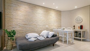 Una sala de estar moderna con pared de piedra, sofá gris, sillas blancas y una mesa de comedor con un plato decorativo.