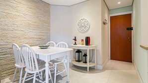 Un comedor con una mesa y sillas blancas, una pared decorativa, una pequeña mesa con faroles y una puerta de madera.