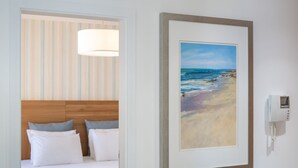 Una habitación de hotel con una cama, un cuadro de una playa, un teléfono y una lámpara.