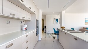Una cocina moderna con armarios blancos, una cafetera y una zona de comedor con una silla azul y un portátil sobre la encimera.