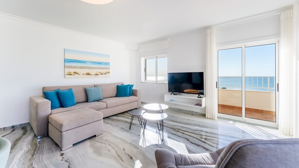 Una sala de estar con un sofá color beige, un televisor de pantalla plana y un cuadro de una playa.