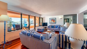 A modern living room with striped sofas, a flat-screen TV, and a view of the marina.