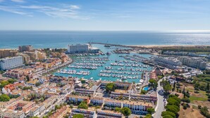 A coastal town with a marina filled with boats, surrounded by residential buildings and a large hotel.