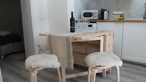 A small kitchen with a wooden table, two cushioned stools, a wine bottle, and a microwave. - Casa das Bonecas by LovelyStay (Évora Monte)