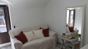 A white sofa with red pillows, a small table with a tray of items, and a mirror reflecting the room. - Casa das Bonecas by LovelyStay (Évora Monte)