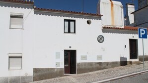 A white building with a tiled roof, a door, and a window with a shutter. - Casa das Bonecas by LovelyStay (Évora Monte)