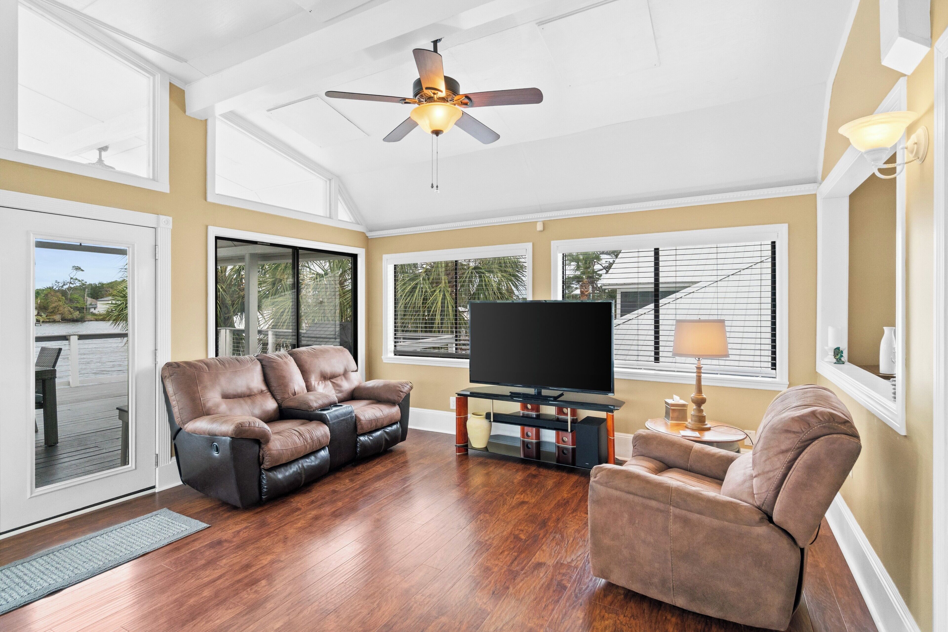 A spacious living room with a ceiling fan, a flat-screen TV, leather sofas, and a wooden floor.