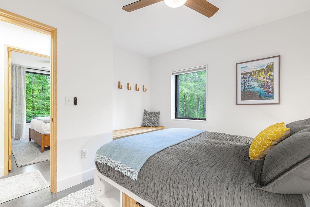 Een moderne slaapkamer met een groot bed, een raam met uitzicht op bomen, een plafondventilator en een schilderij aan de muur.