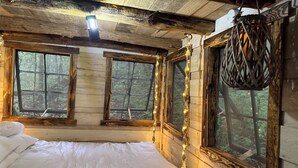 A rustic wooden cabin bedroom with a bed, two windows, and a hanging lantern. - Unplug and hide from the world in this rustic South Pittsburg cabin (South Pittsburg)