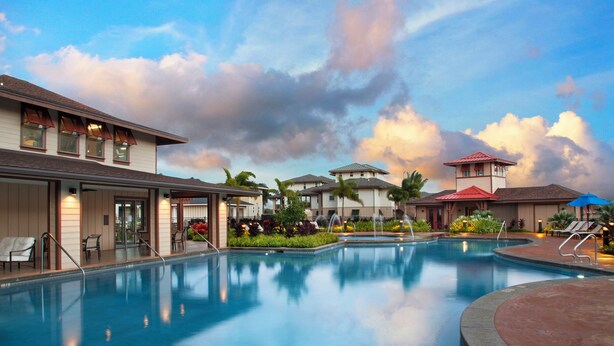A swimming pool with lounge chairs and umbrellas, surrounded by buildings with a tropical architectural style.