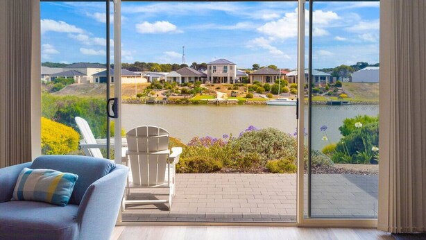 A room with a large sliding glass door leading to a scenic outdoor view of a lake, houses, and greenery.