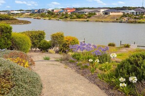 A lakeside residential area with houses, a gravel path, and various flowering plants. - Hindmarsh Island - Pelicans on Parade (Hindmarsh Island)