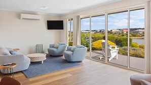 A modern living room with a large sliding glass door leading to a deck with a view of a lake and houses.