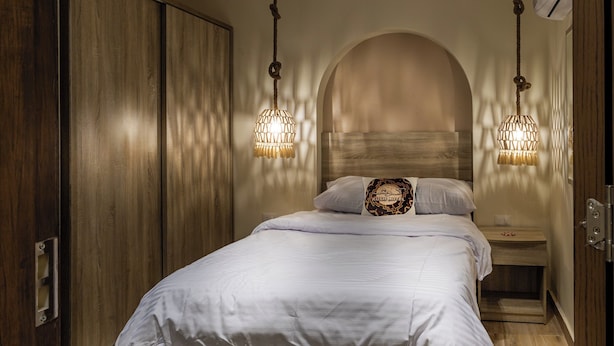Un dormitorio con un armario de madera, una cama con ropa de cama blanca y dos lámparas colgantes.