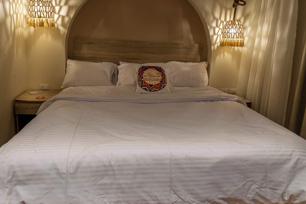 A neatly made bed with a decorative pillow, a wooden headboard, and two wall-mounted lamps.