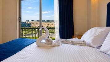 A hotel room with a bed, a swan-shaped towel arrangement, a view of a cityscape through a large window, and a dark curtain.