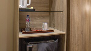 Una kitchenette compacta con nevera integrada, cafetera y una botella de agua sobre la encimera.
