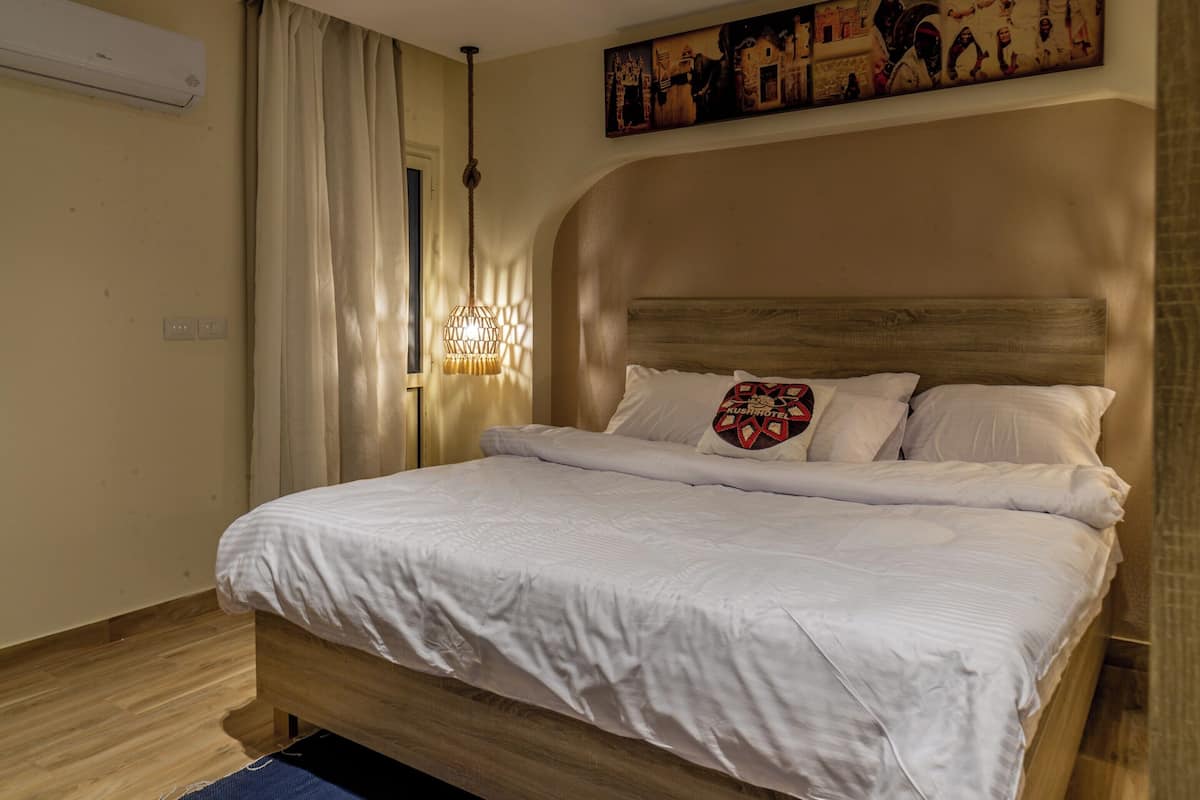 A neatly made bed with white linens, a wooden headboard, and a decorative pillow.