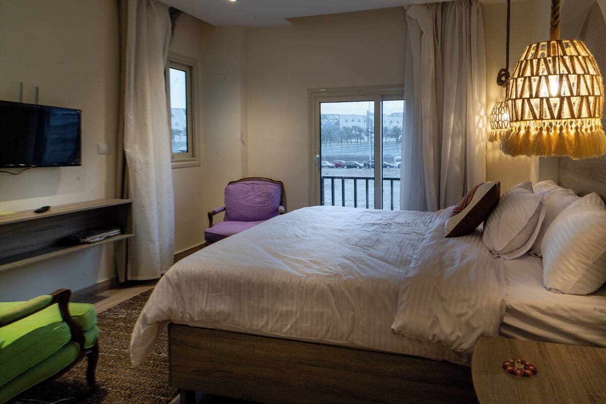 A hotel room with a bed, a chair, a TV, and a balcony with a view.
