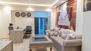 Un moderno vestíbulo de hotel con una recepción, un espacio de estar cómodo con un sofá y sillones, y un cartel grande en la pared.