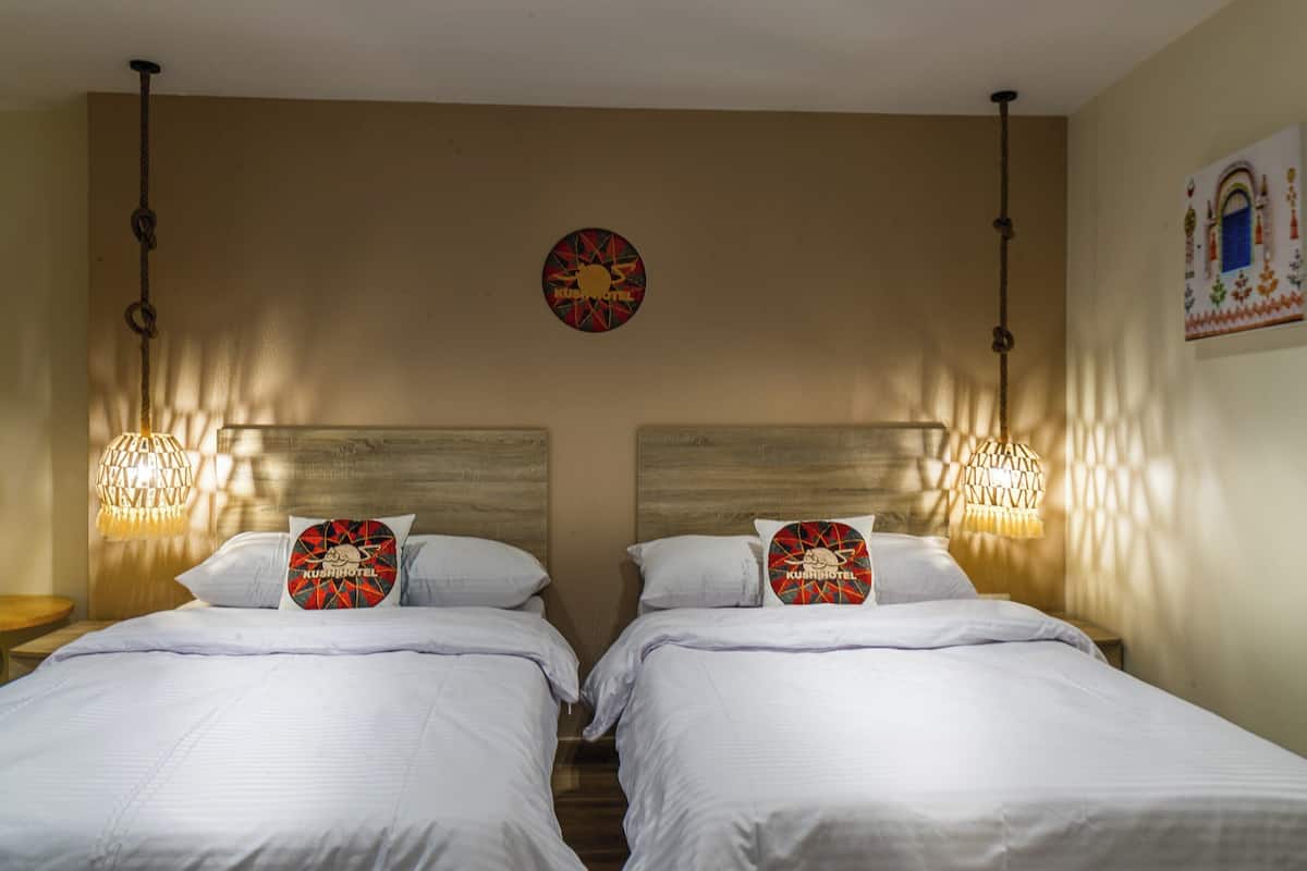 A hotel room with two beds, each with a pillow featuring a logo. There is a wall clock and a decorative wall hanging.