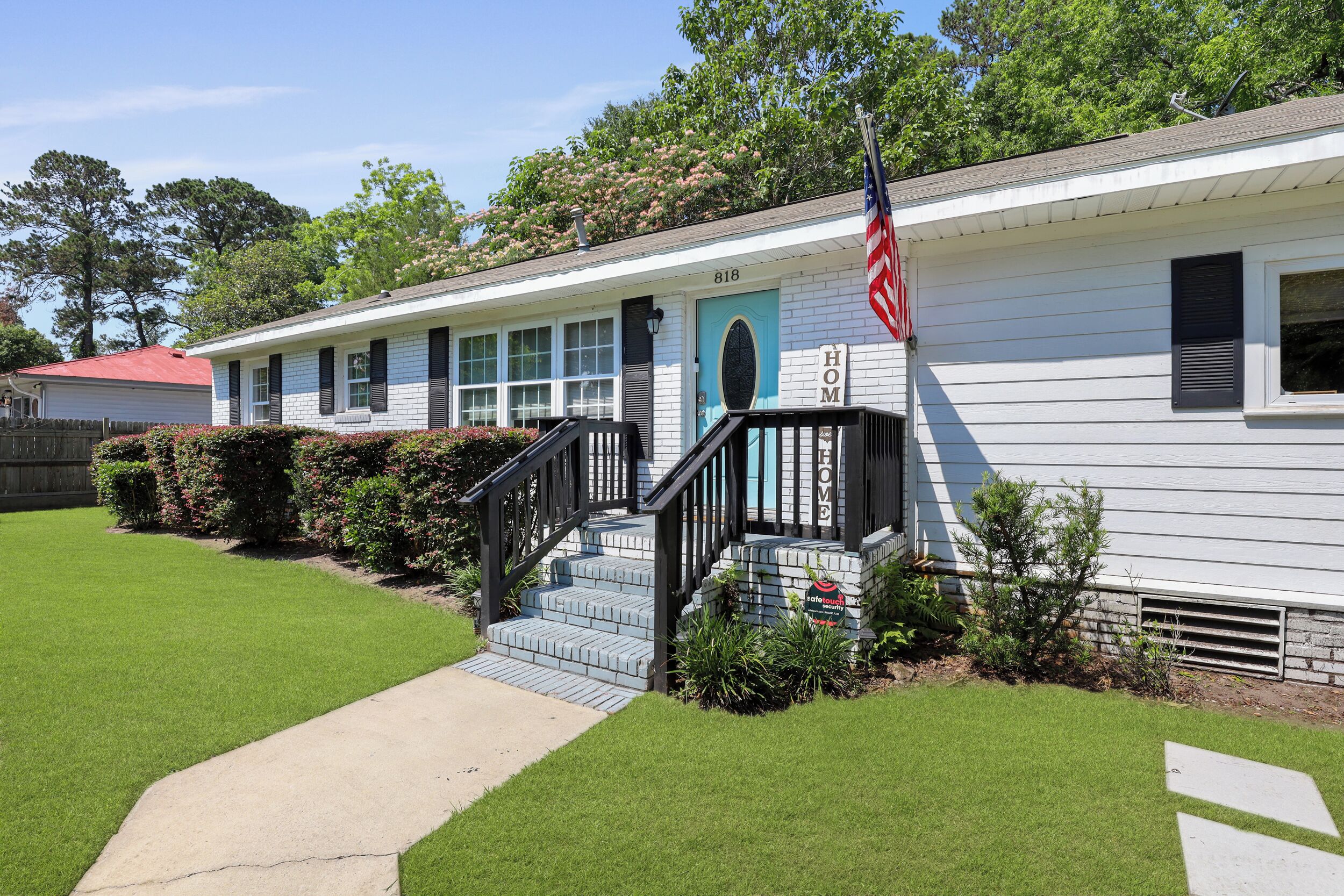 A white single-story house with a blue door, a front porch, and a small staircase leading to the entrance.