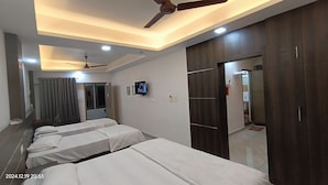 Camera d'albergo con tre letti, una ventola a soffitto, illuminazione incassata, televisione e un armadio.