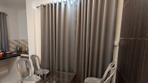 Un piccolo angolo living con un tavolino in vetro, due sedie di plastica e una tenda scura.