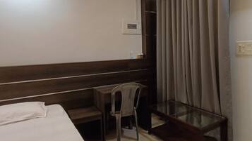 A hotel room with a bed, a small table, a chair, a wardrobe, and a curtain.