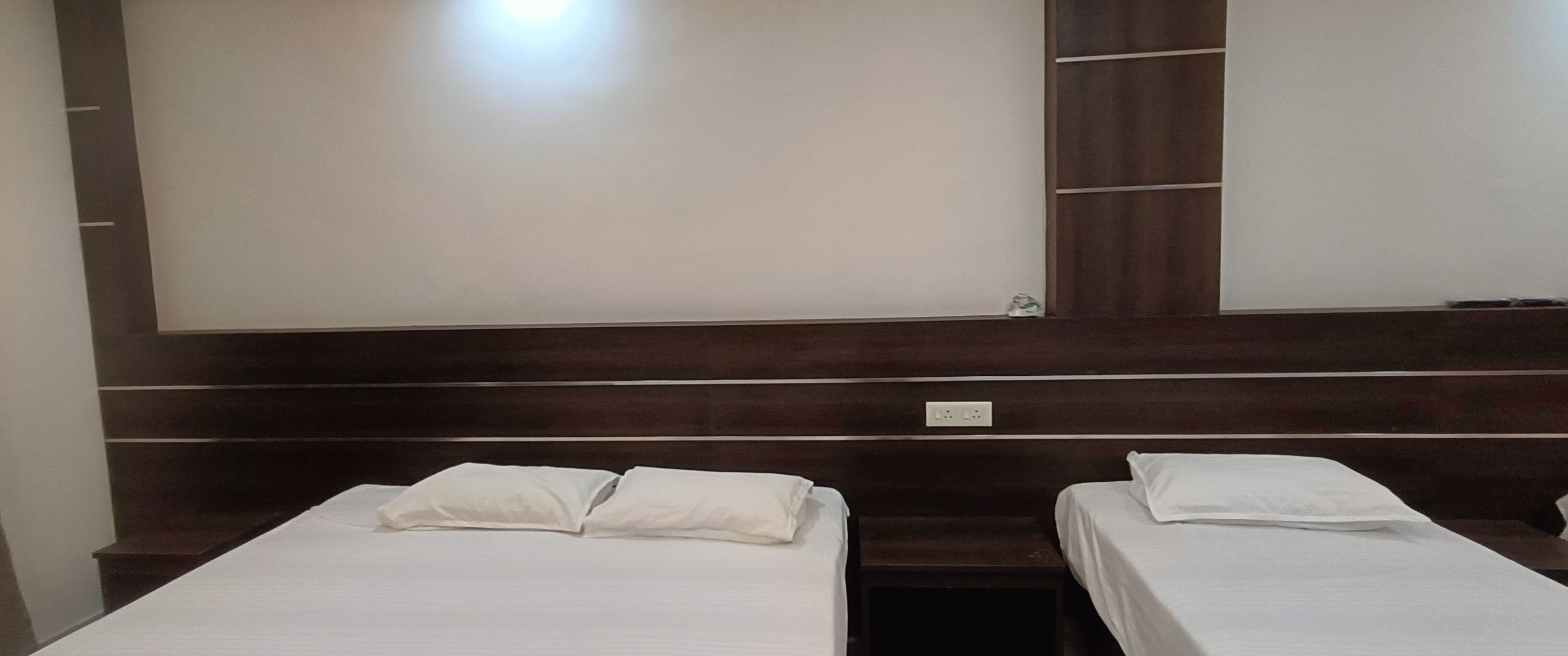 A hotel room with two single beds, a wooden headboard, a large mirror, and a wall socket.