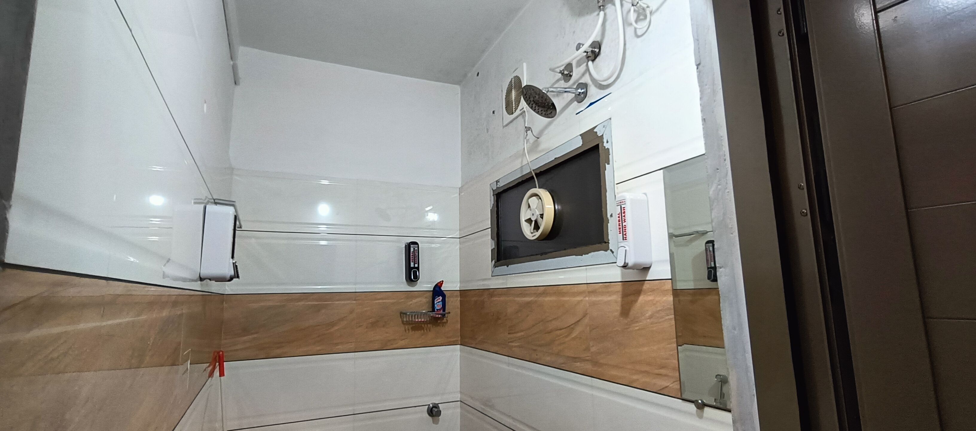 A bathroom with a white and brown tiled wall, a mirror, a towel dispenser, and a toilet.