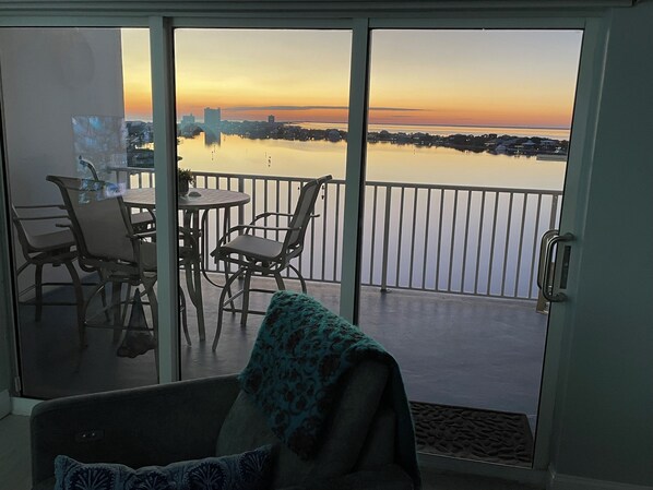 A balcony with a view of a calm body of water and a city skyline at sunset.