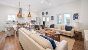 Ein großzügiger Wohnbereich mit Sofa, Sesseln und Couchtisch. Es gibt eine Essecke mit Tisch und Stühlen, und im Hintergrund befindet sich eine Küche.
