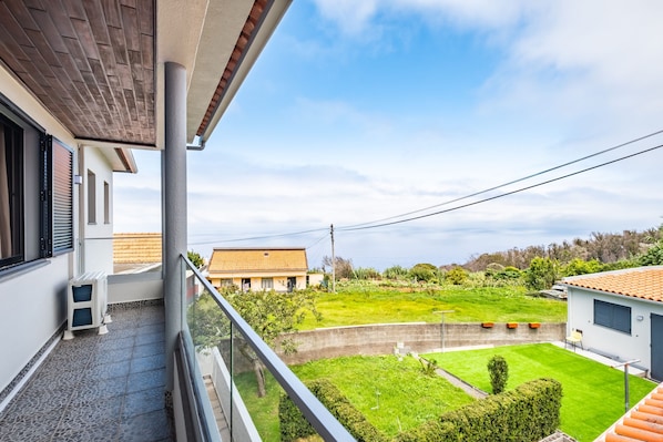 A balcony with a view of a well-maintained lawn and neighboring houses. - Cozy Apartment 2 by Homie (Porto Moniz)