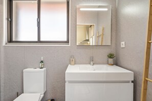 A modern bathroom with a toilet, a sink, and a mirror. - Cozy Apartment 2 by Homie (Porto Moniz)