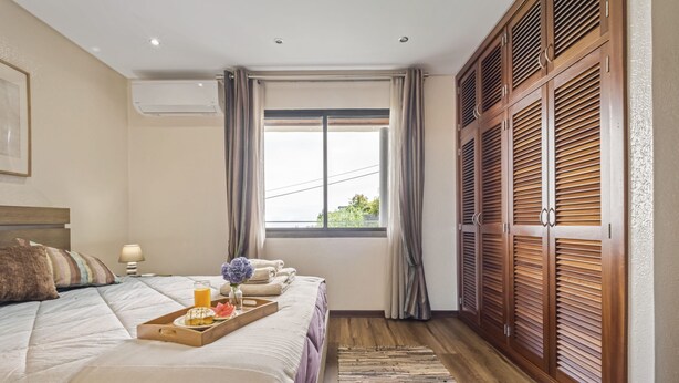 A hotel room with a large bed, a wooden wardrobe, a window with curtains, and a tray with breakfast items. - Cozy Apartment 1 by Homie (Porto Moniz)