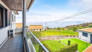 A balcony with a view of a well-maintained lawn and neighboring houses. - Cozy Apartment 1 by Homie (Porto Moniz)