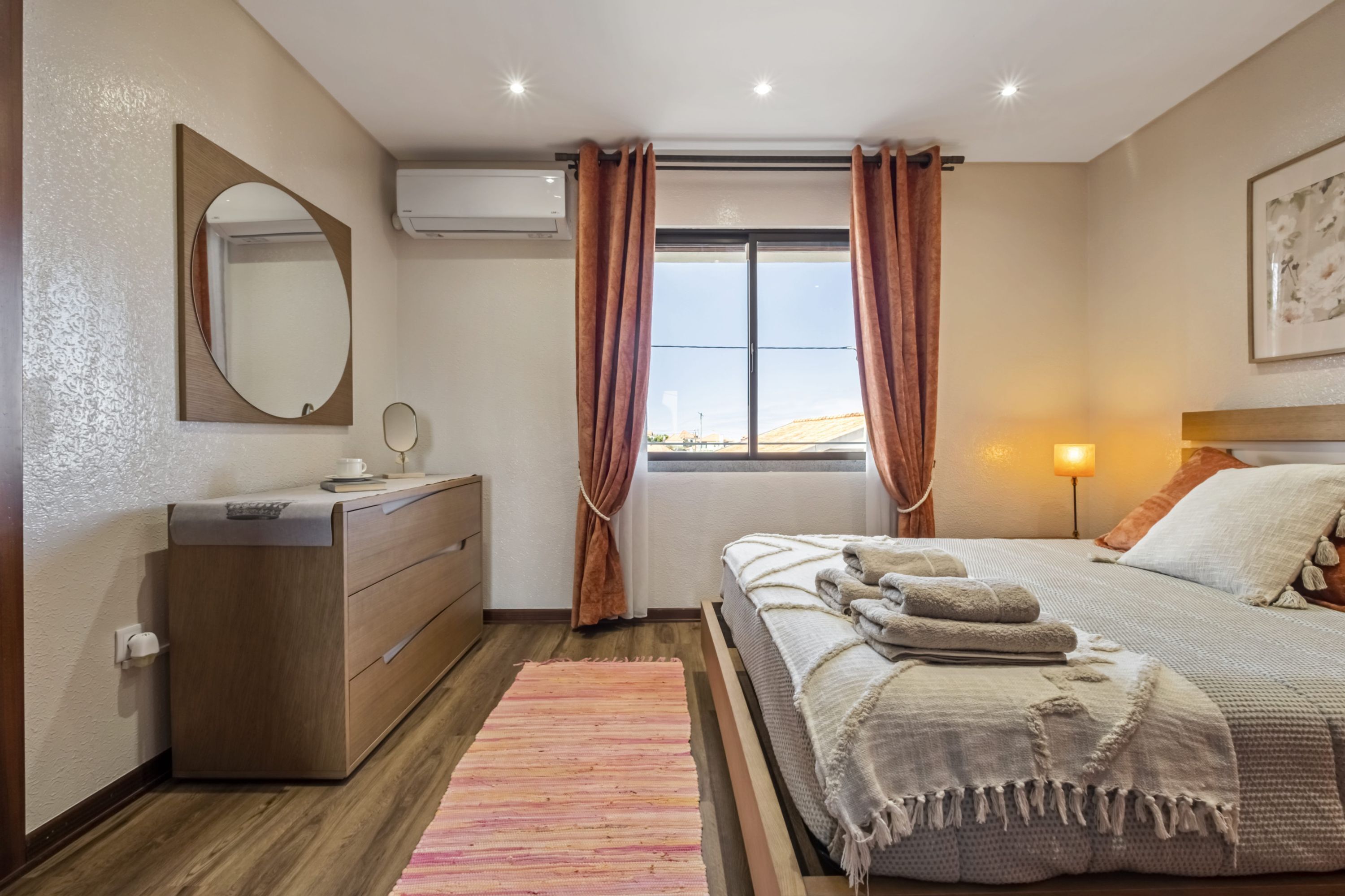 Quarto com cama, cômoda, espelho e janela com cortinas.