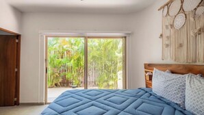 A bedroom with a large bed, a sliding glass door to a balcony, and a wooden headboard.
