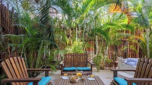A wooden deck with a table and chairs, surrounded by dense tropical foliage.
