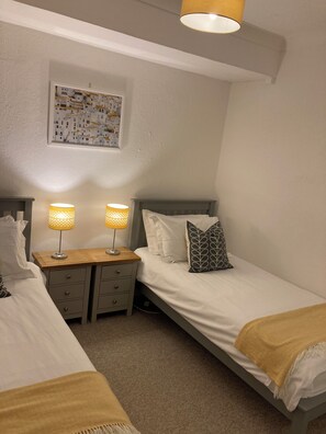 A small, well-lit bedroom with two beds, a nightstand, and a wall-mounted lamp.
