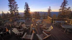 Eine Terrasse mit Außenmöbeln und einem Feuerkorb, umgeben von hohen Bäumen und Blick auf die Berge.